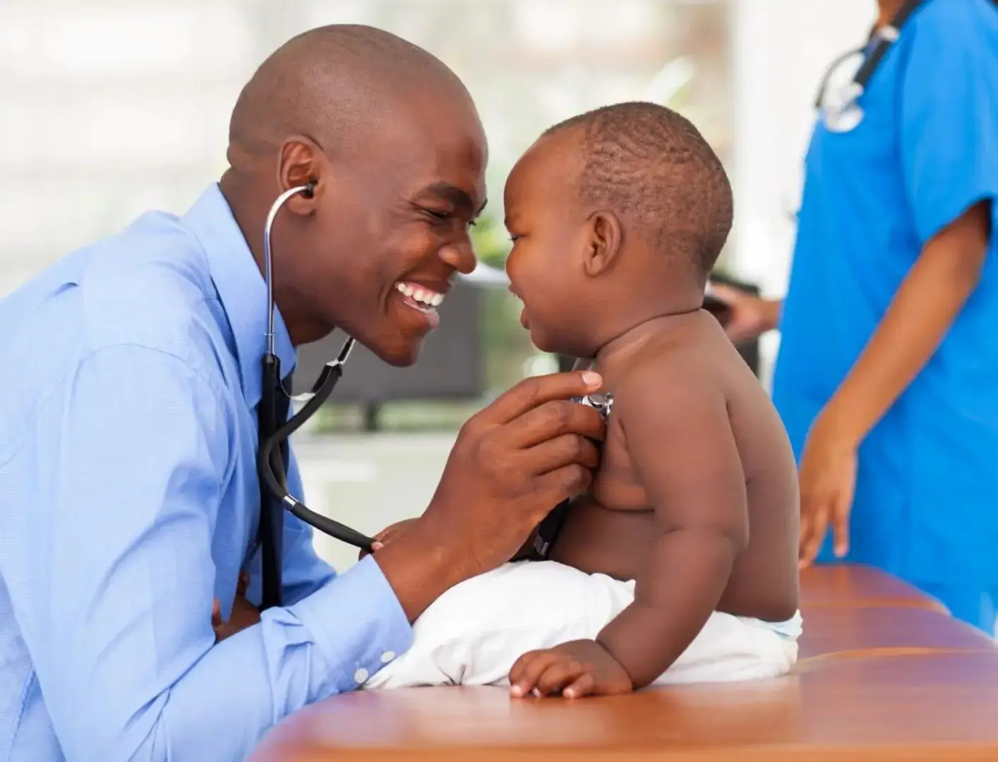 A doctor is holding a baby and smiling.