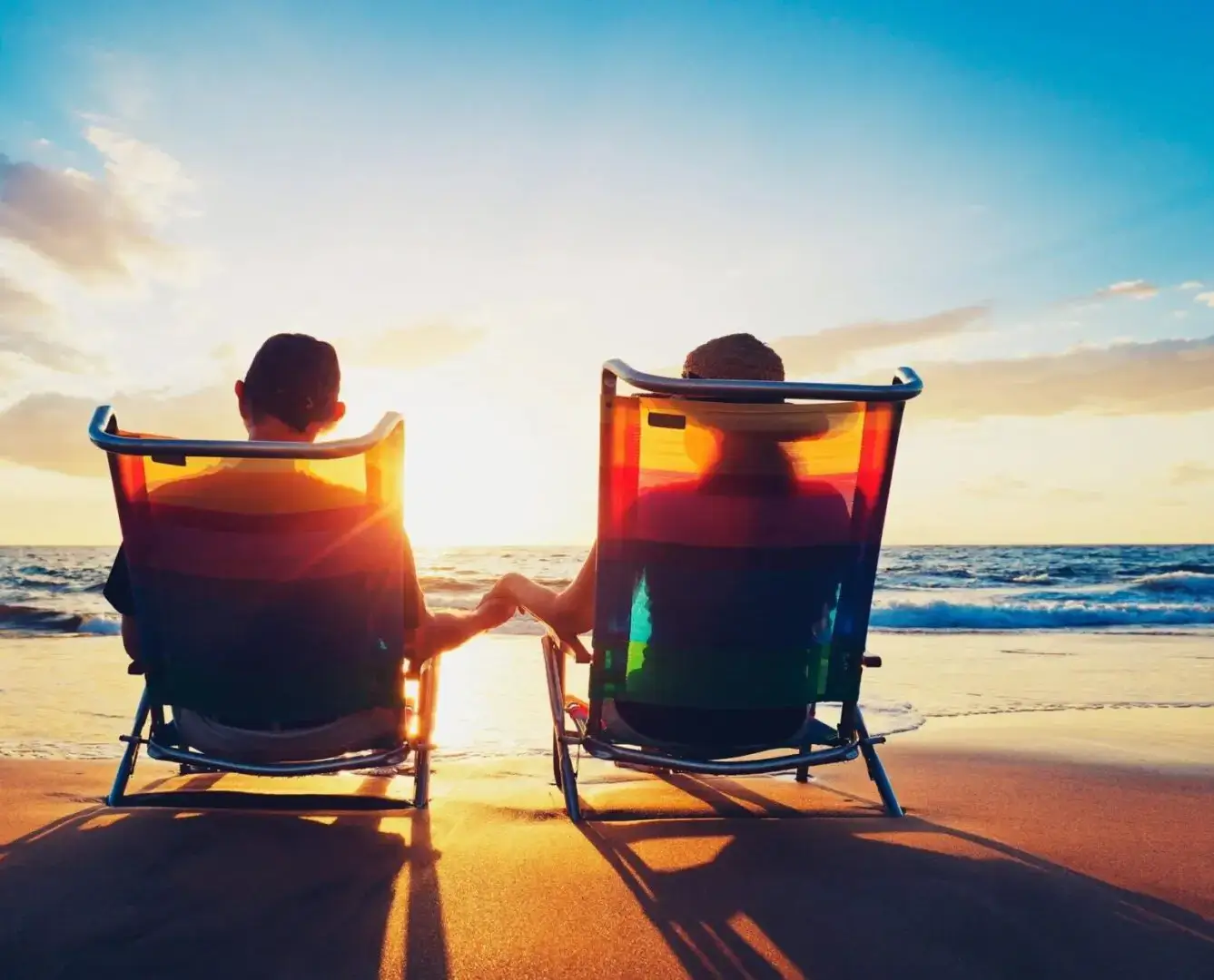 Two people sitting in lawn chairs on the beach